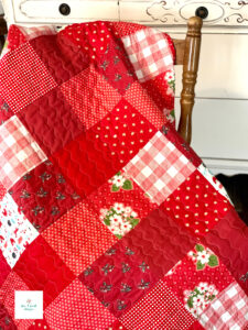 Red scrappy patchwork quilt draped over chair.