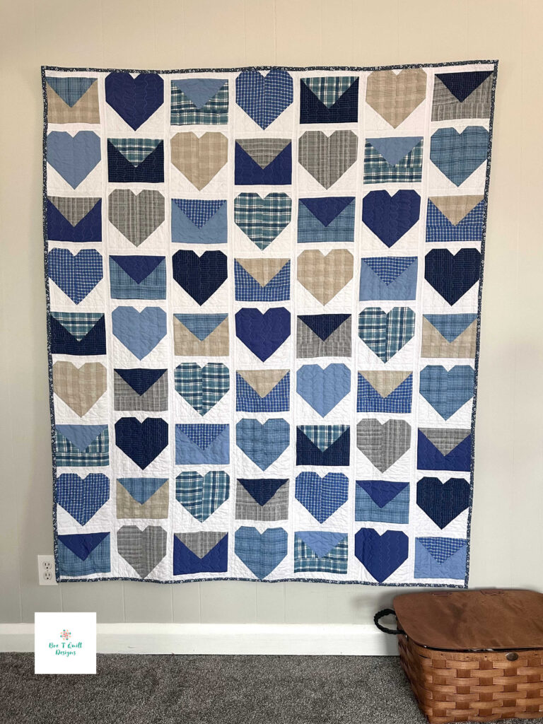Love Letters Memory Quilt- Bre T Quilt Designs copy 3 The completed Love Letters quilt displayed vertically, showing the repetitive pattern of hearts and envelopes created from sentimental clothing in shades of blue, grey, and plaid.