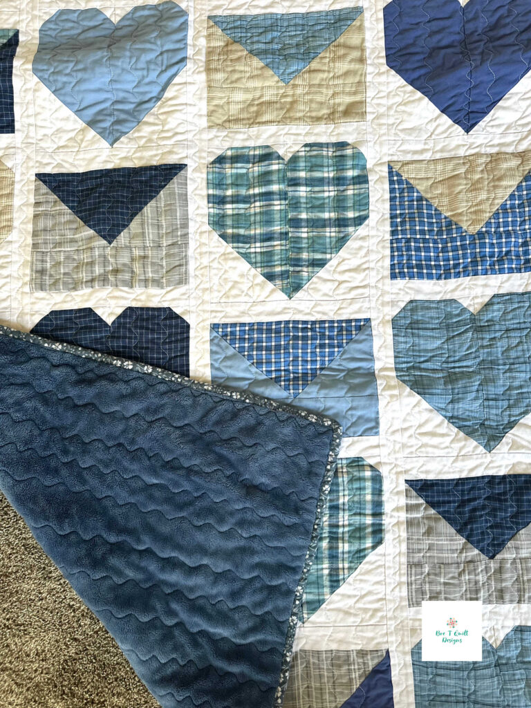 Love Letters Memory Quilt- Bre T Quilt Designs copy 5 A corner of the heart memory quilt folded over to reveal a soft, plush blue minky backing, emphasizing the cozy and comforting weight of the blanket.