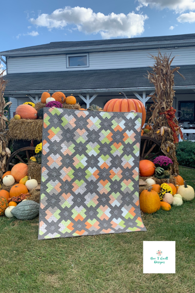 Finished fall jelly roll quilt with oranges, greens, and greys featured in front of a pumpkin fall display