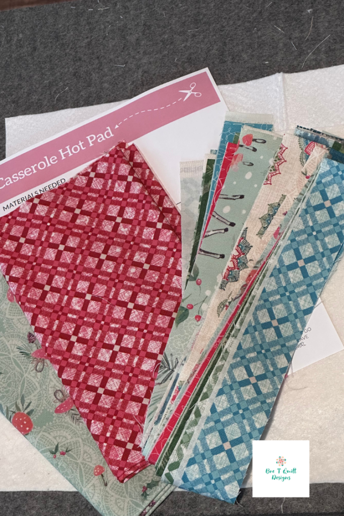 Flat lay of supplies for the quilt-as-you-go hot pad project including strips of Winter Haven fabric, batting, background fabric, and the free pattern