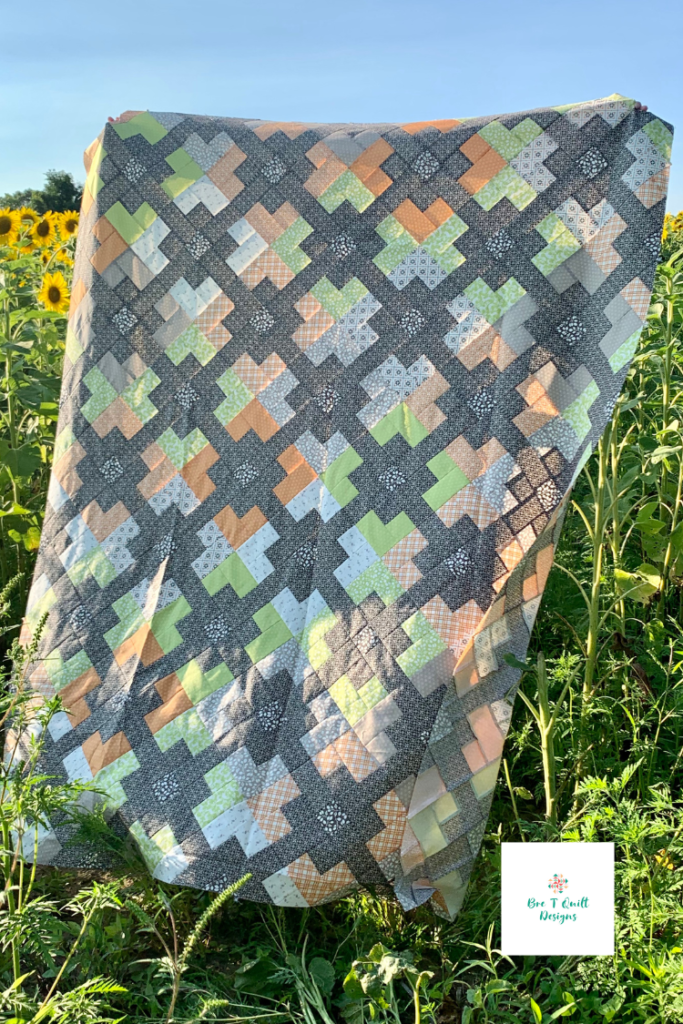 fall jelly roll quilt top with oranges, greens, and greys featured in front of a sunflower fields