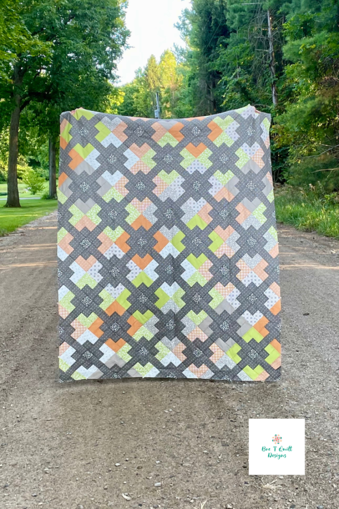  fall jelly roll quilt top with oranges, greens, and greys featured on an empty dirt road surrounded by trees. 