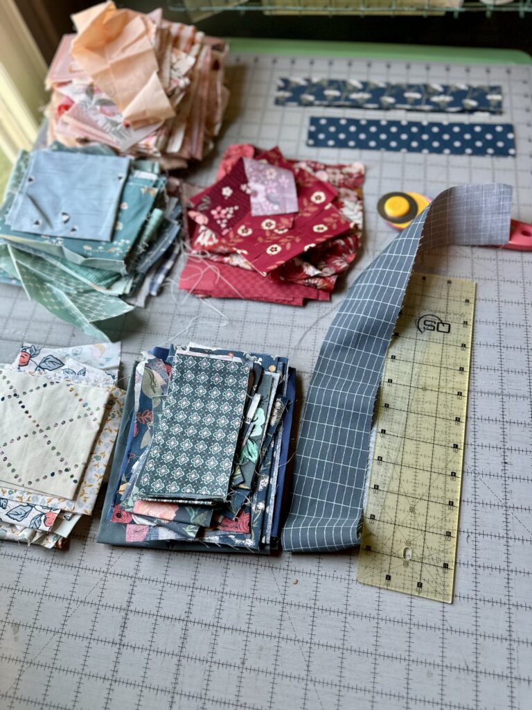 Stacks of red, blue, peach, and low volume scraps for a log cabin scrap quilt